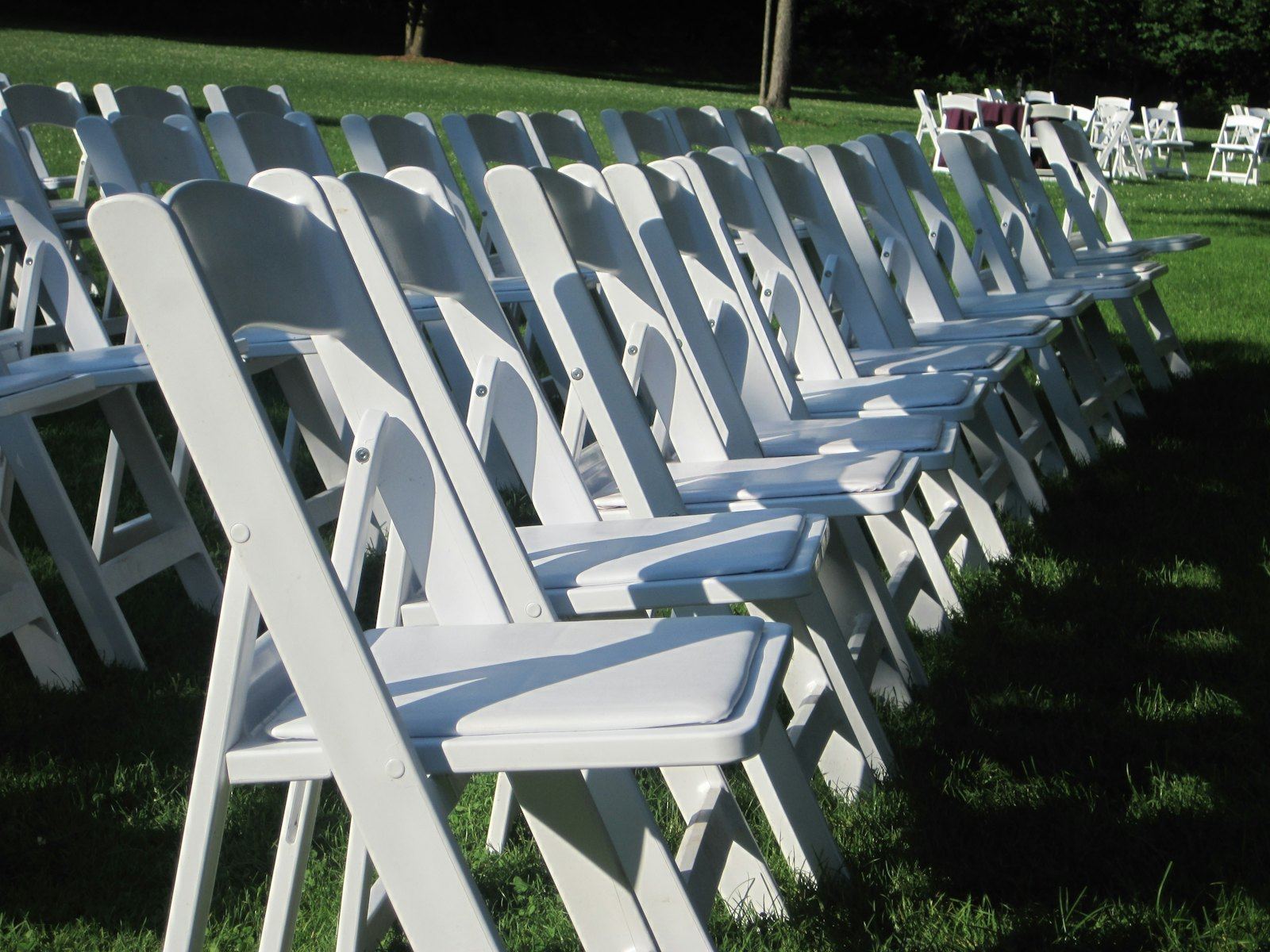 Rows of white folding chairs set on a lawn